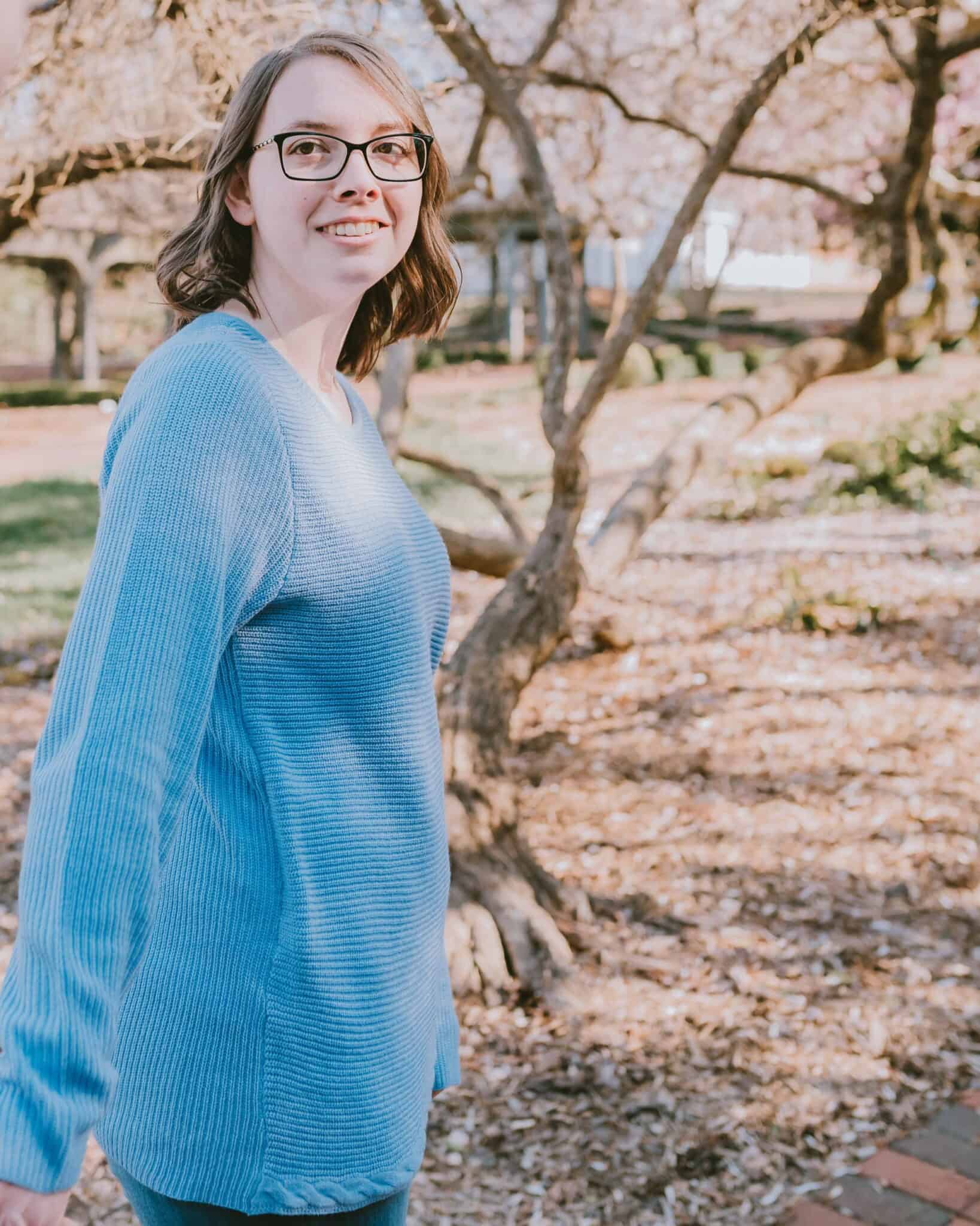 Woman in blue sweater enjoying springtime outdoors with blooming trees.